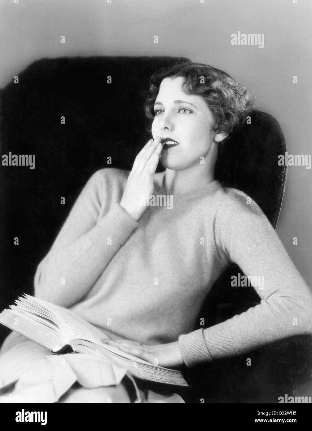 Young woman sitting on a armchair with a book Stock Photo - Alamy