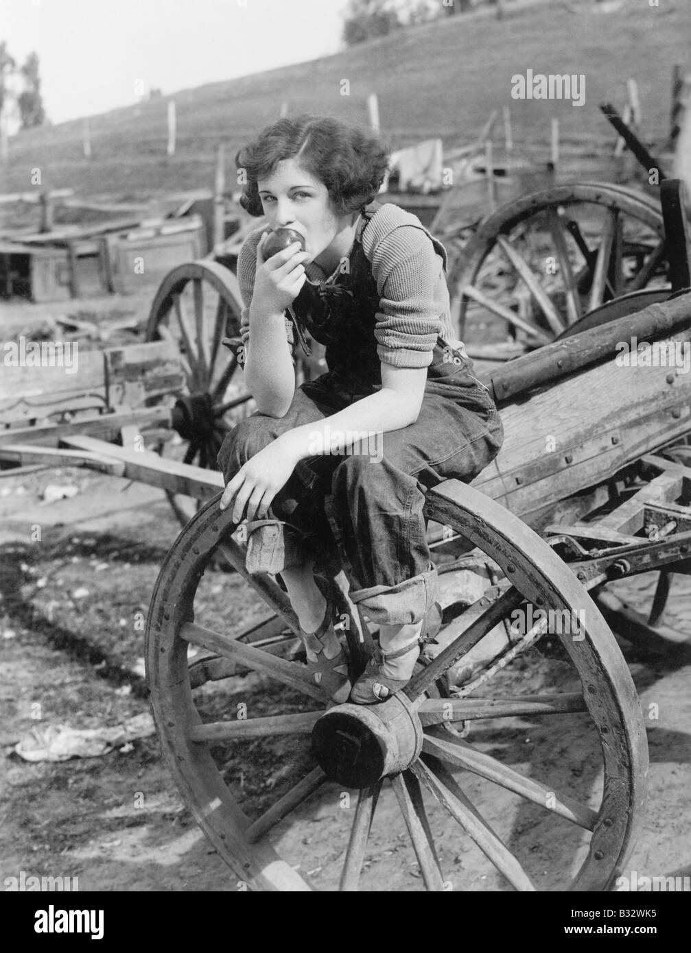 Young woman in working jeans sitting on wheel eating an apple Stock ...