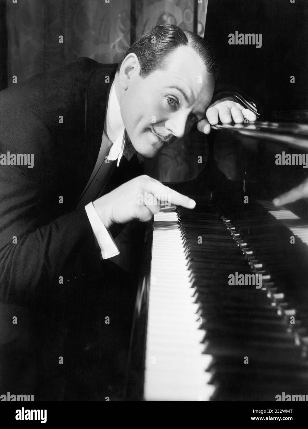 Man leaning over the piano playing the keys with one finger Stock Photo