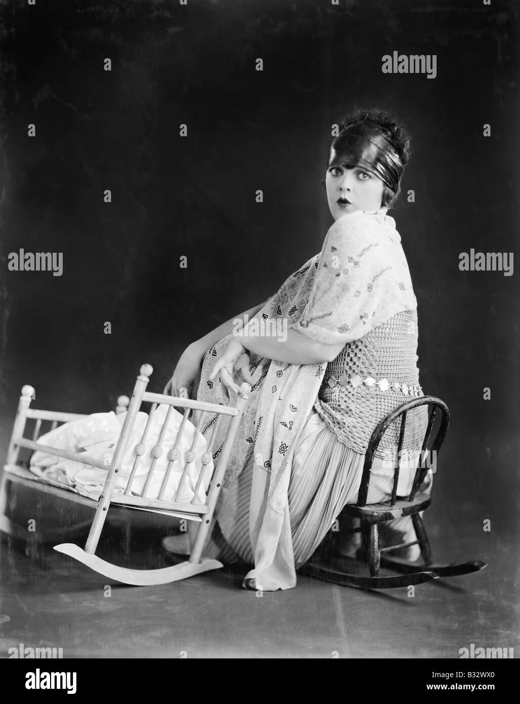 Young woman sitting on a toy chair next to a toy baby crib Stock Photo