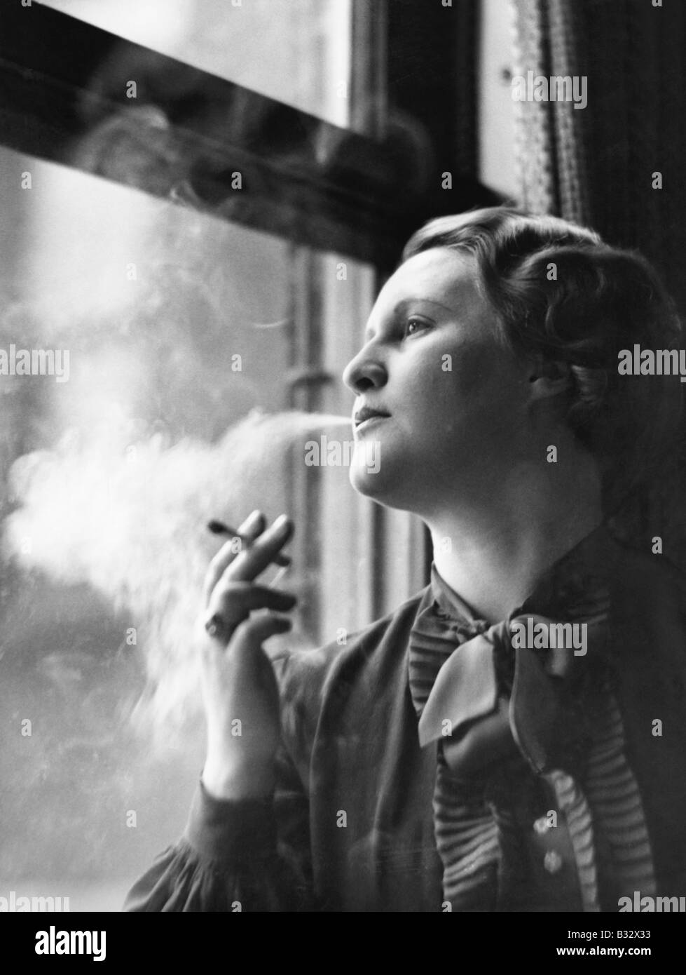 Young woman sitting next to window, smoking Stock Photo