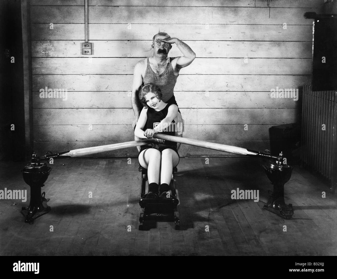 Woman sitting on a rowing machine with a man behind her Stock Photo