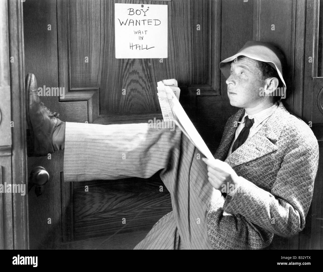 Man leaning against door with his legs up reading newspaper Stock Photo