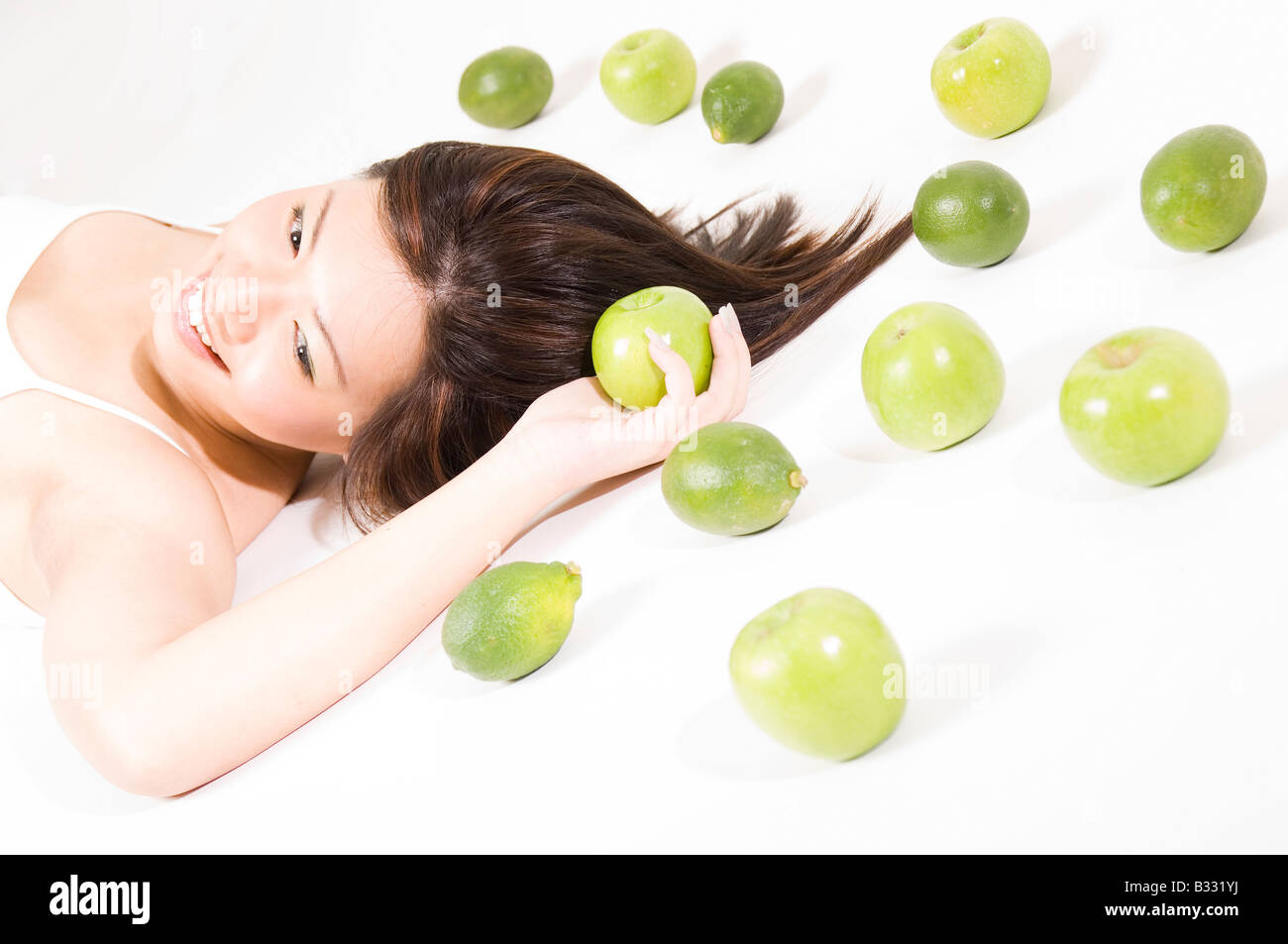 A beautiful young asian woman lies on a white floor holding an apple Stock Photo