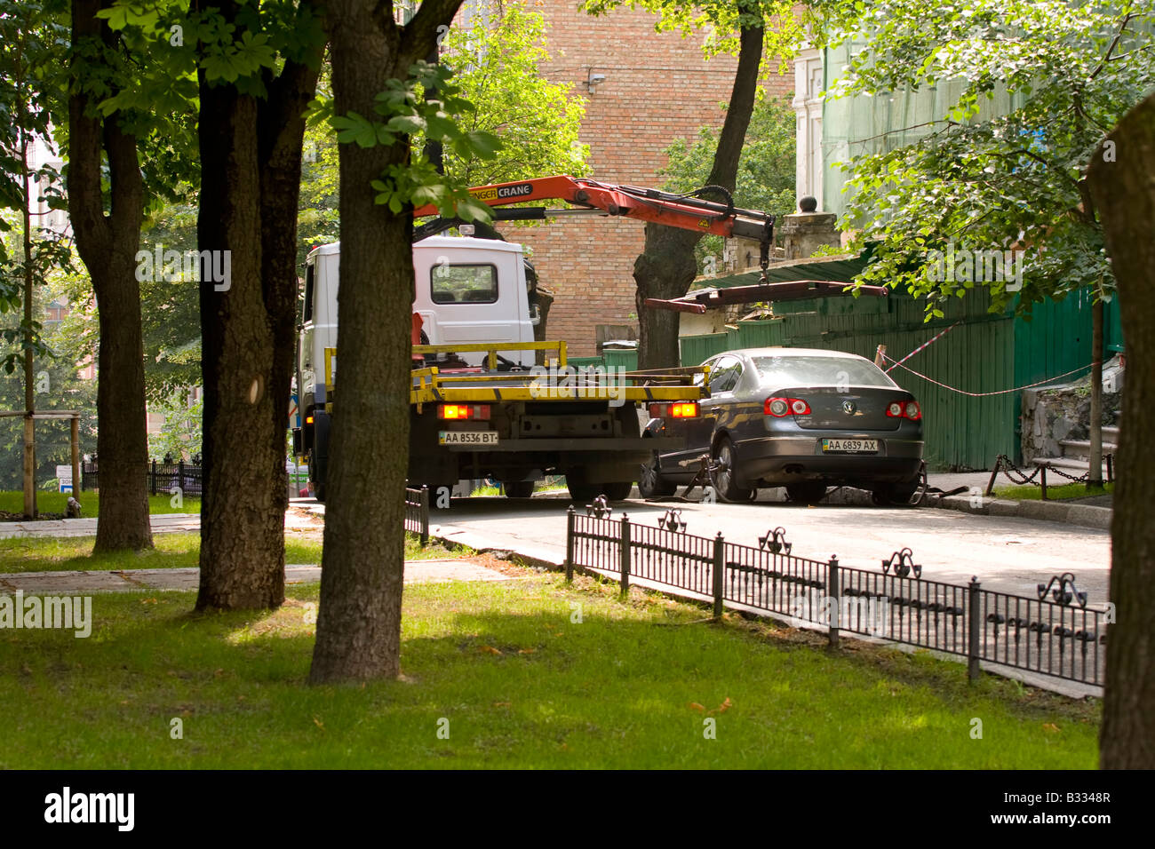 Tow truck lifting a car in an urban park area in Kyiv, surrounded by greenery. Stock Photo