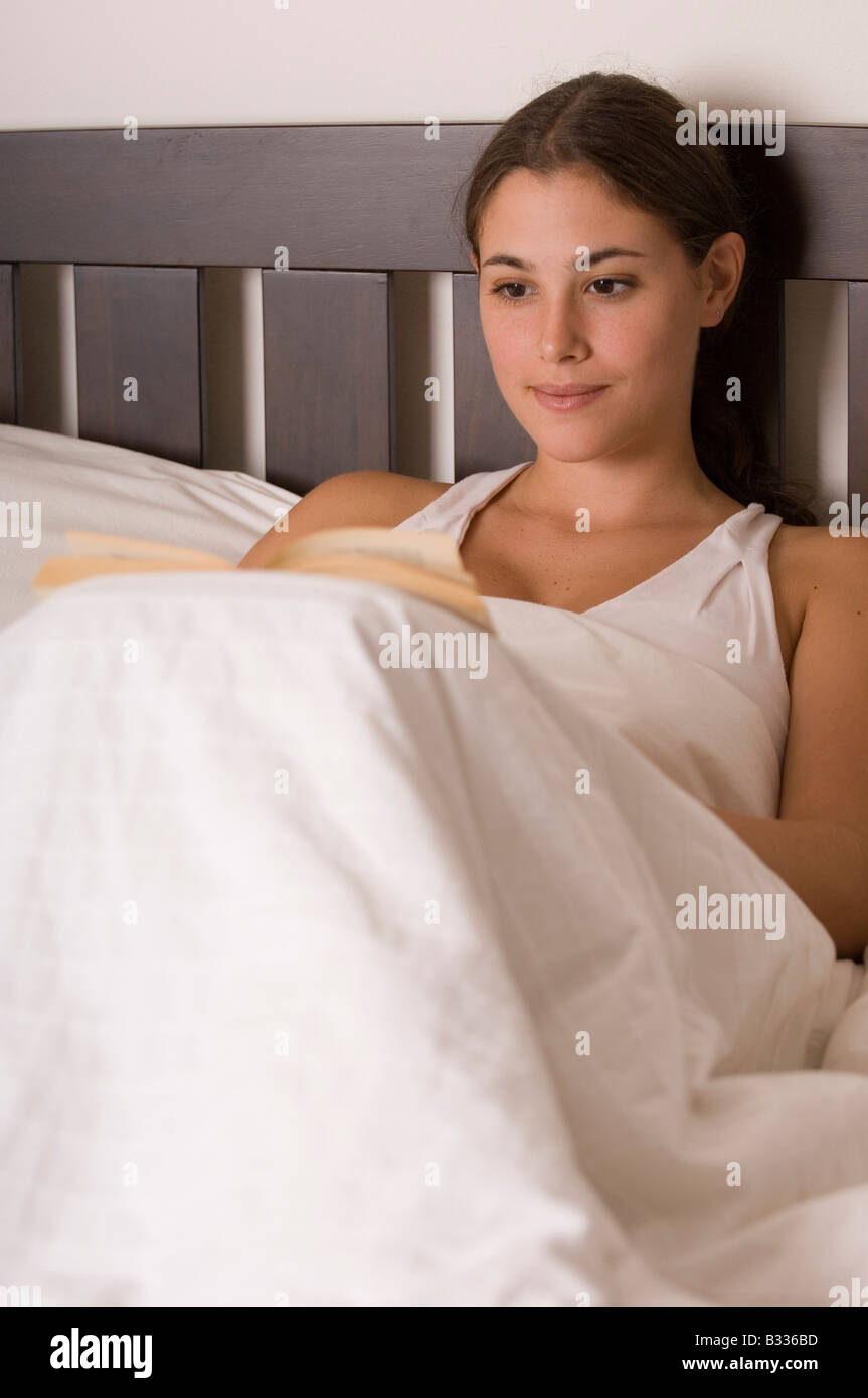 A pretty young woman reads a book in bed Stock Photo Alamy