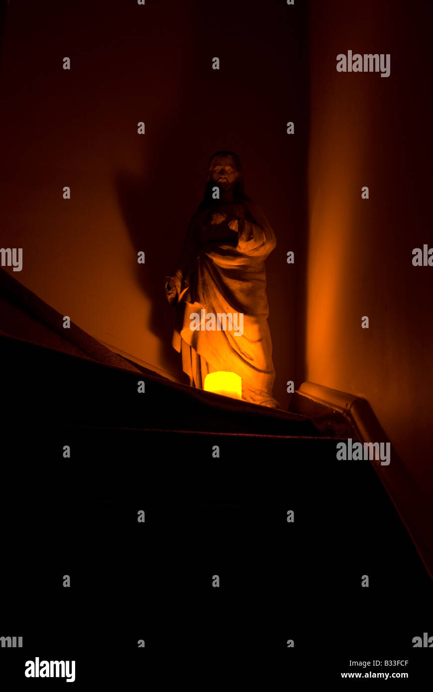 Looking up stairs at a atmospheric shadowy statue of Jesus Christ in amber orange candle glow Stock Photo