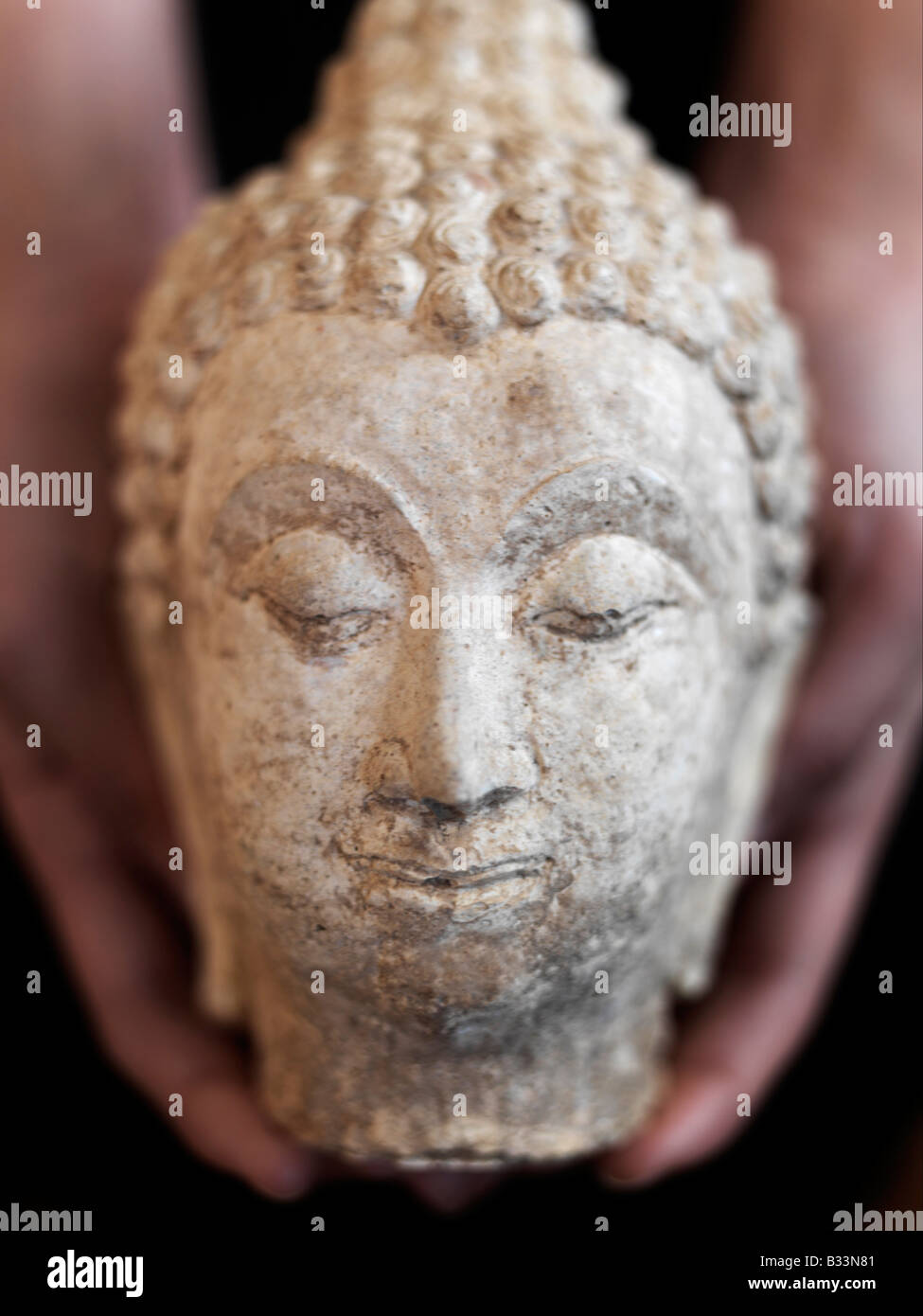 A close up view of female hands hold a statue of a Buddha head Stock Photo