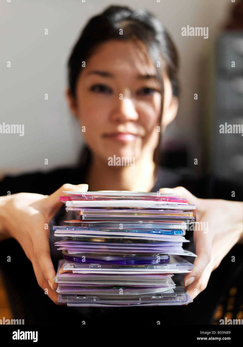 A young Asian woman holds up a stack of CDs Stock Photo