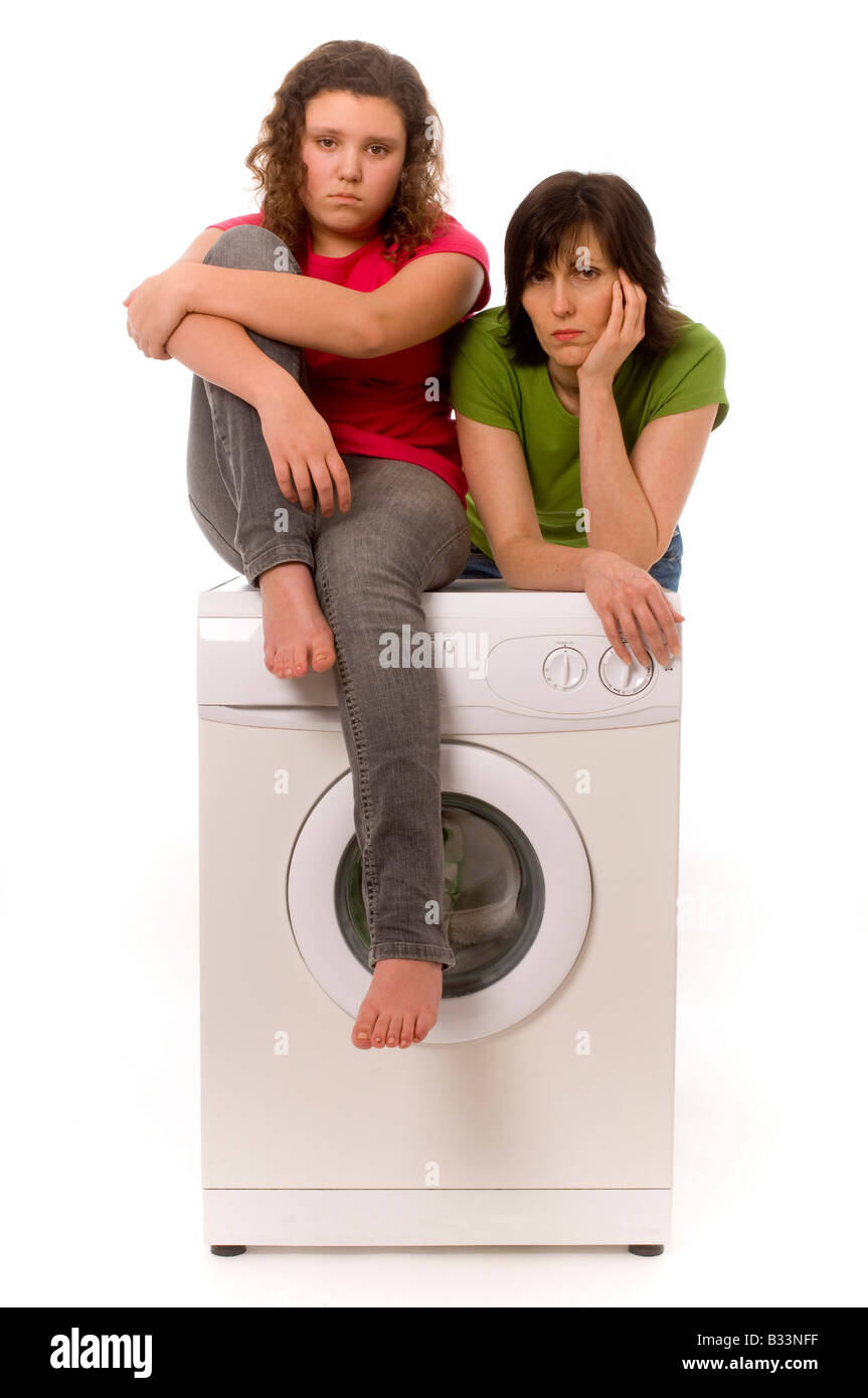 Two casually dressed caucasian females, one leaning and one sitting on a washing machine looking glum. Stock Photo