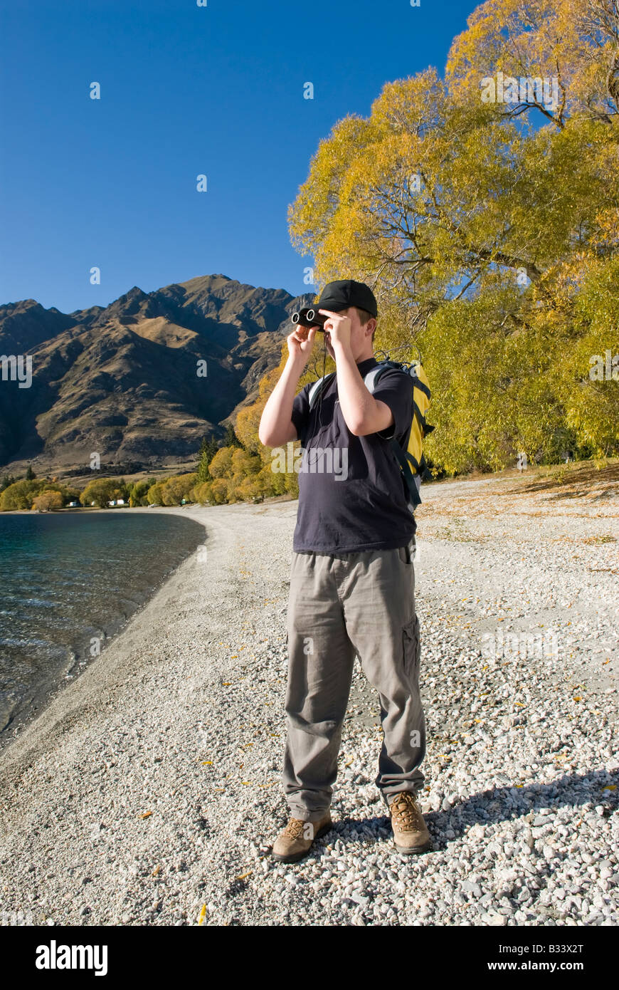Young hiker looking through binoculars at Glendhu Bay on lake shore Stock Photo