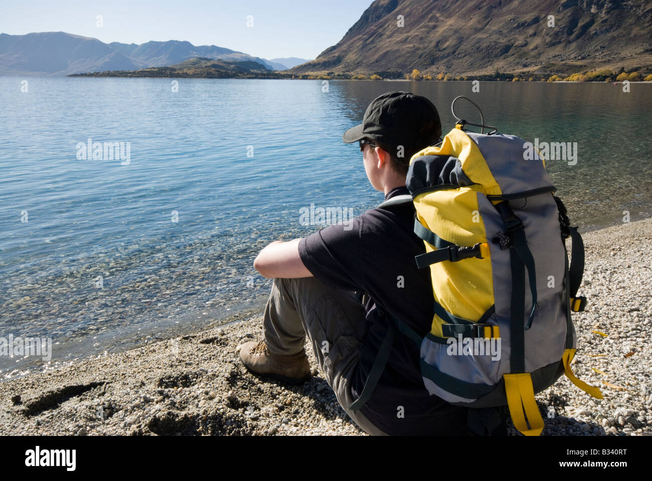 Young hiker sat on lake shore looking out Stock Photo