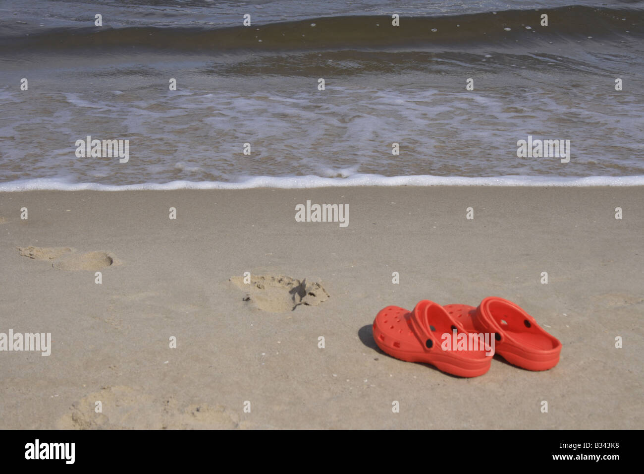 pair of red crocs and human footprint at the sandy beach. Photo by