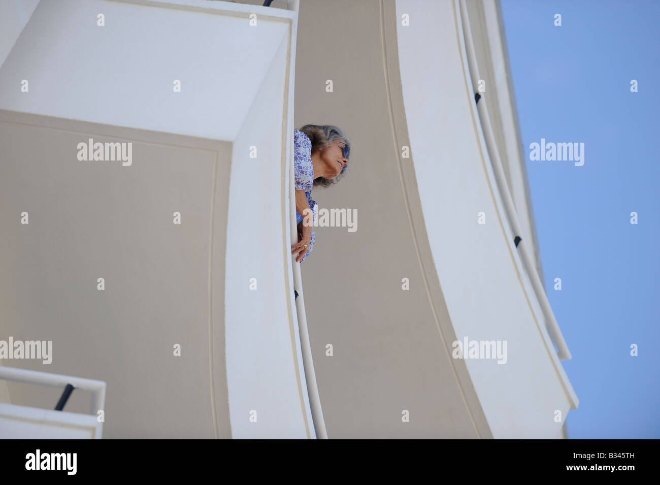 A woman looking out from a modern purpose-built apartment block balcony in Eastbourne, East Sussex. Stock Photo