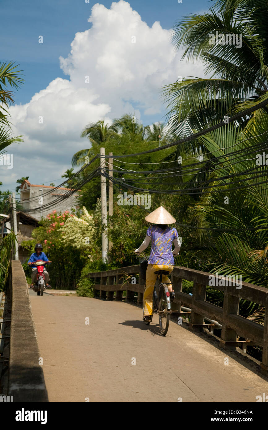 An iconic picture of a vietnamese lady with conical hat cycling over a bridge Stock Photo