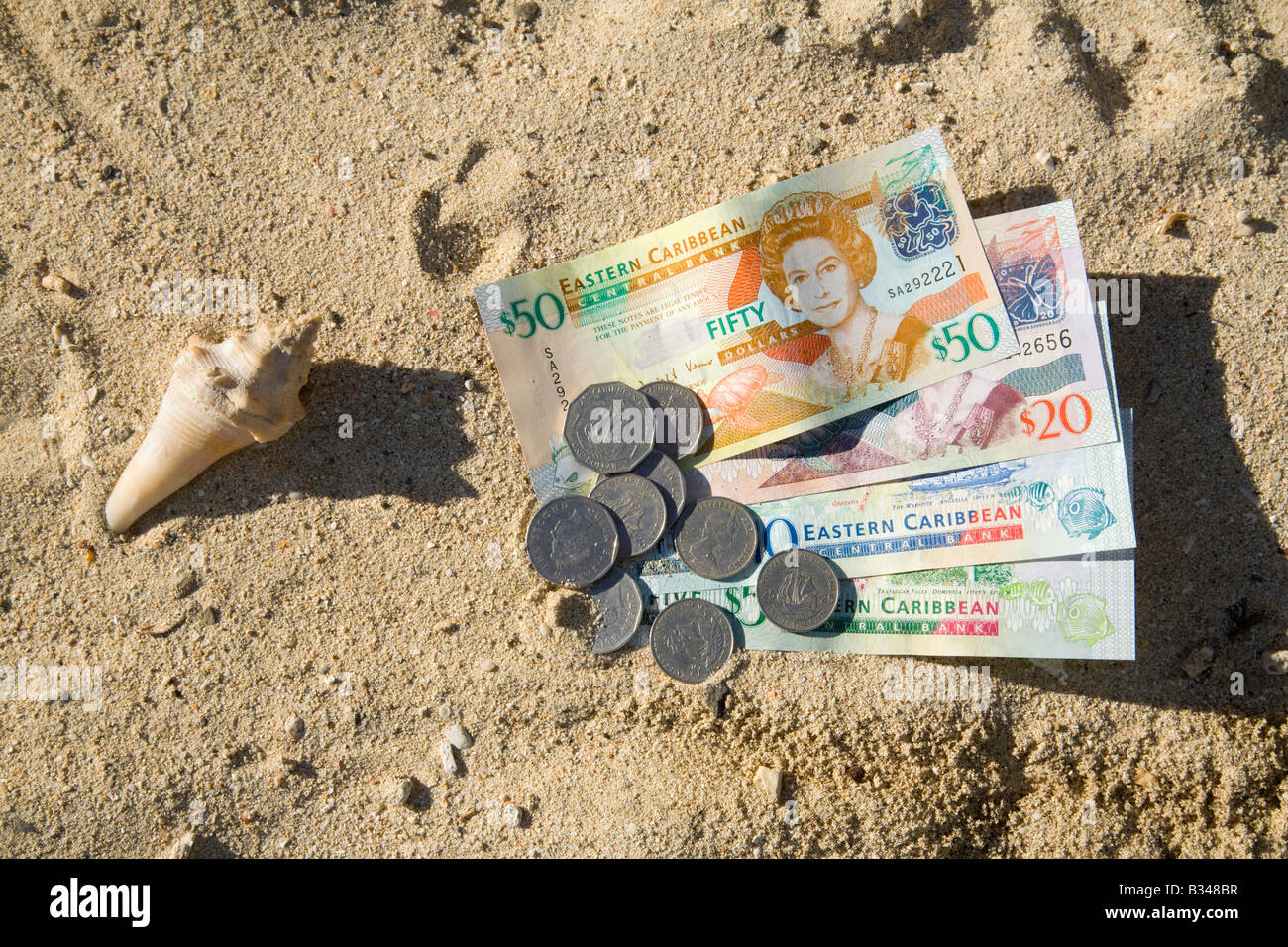 Caribbean money; East Caribbean currency; notes and coins and a shell on the beach, St Lucia, Windward islands, Caribbean, West Indies Stock Photo