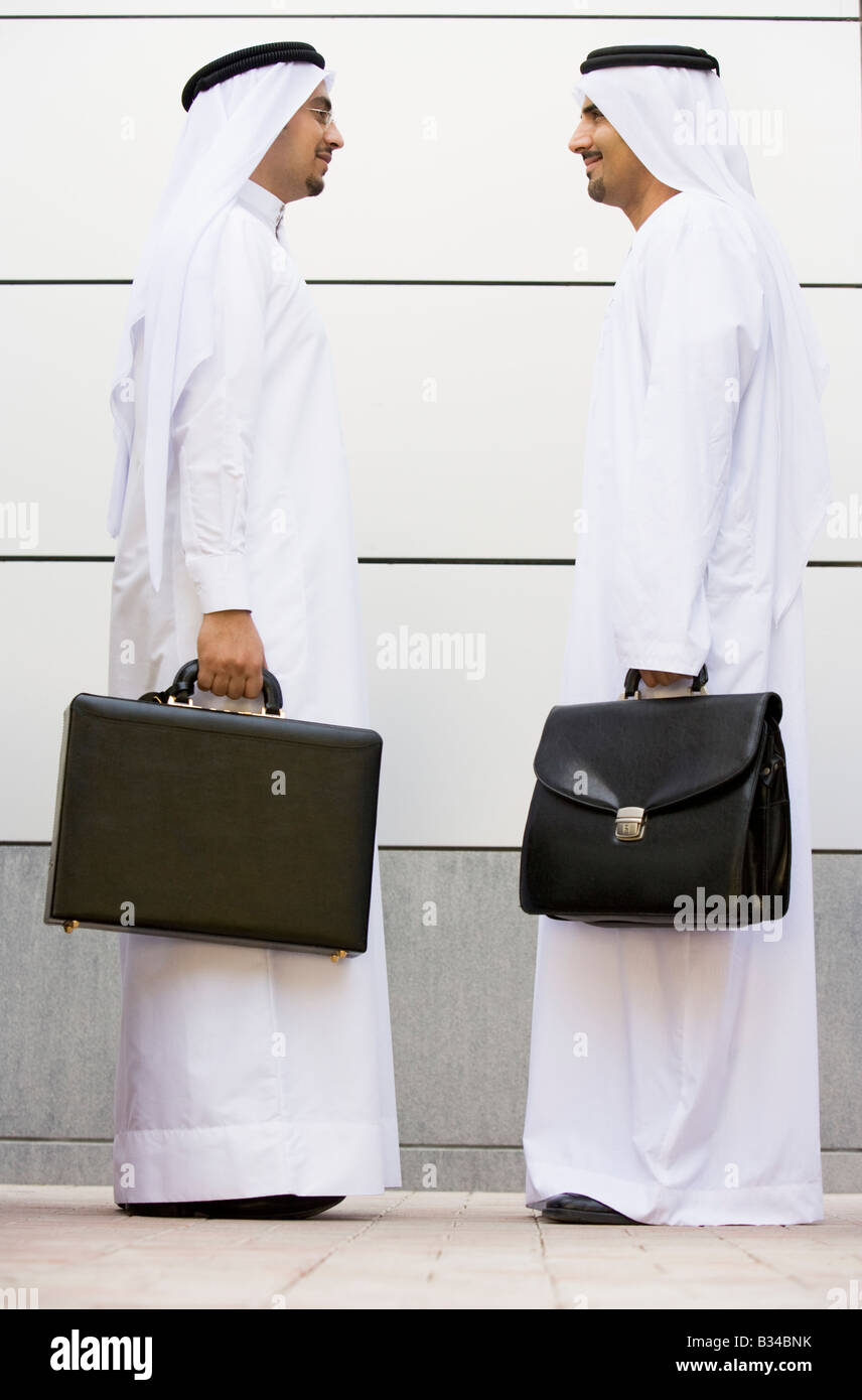 Two businessmen standing outdoors with briefcases smiling Stock Photo