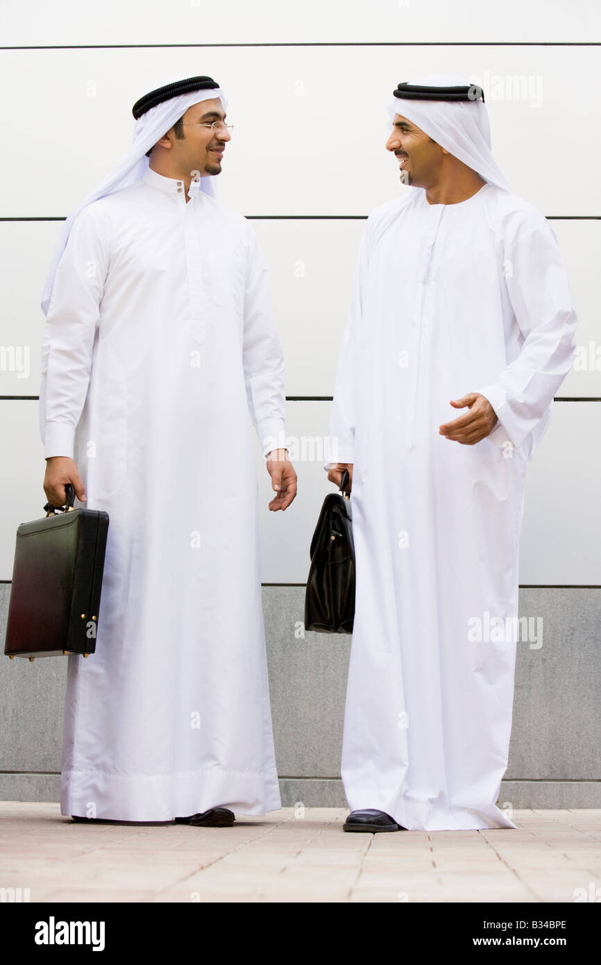 Two businessmen standing outdoors with briefcases talking and smiling Stock Photo