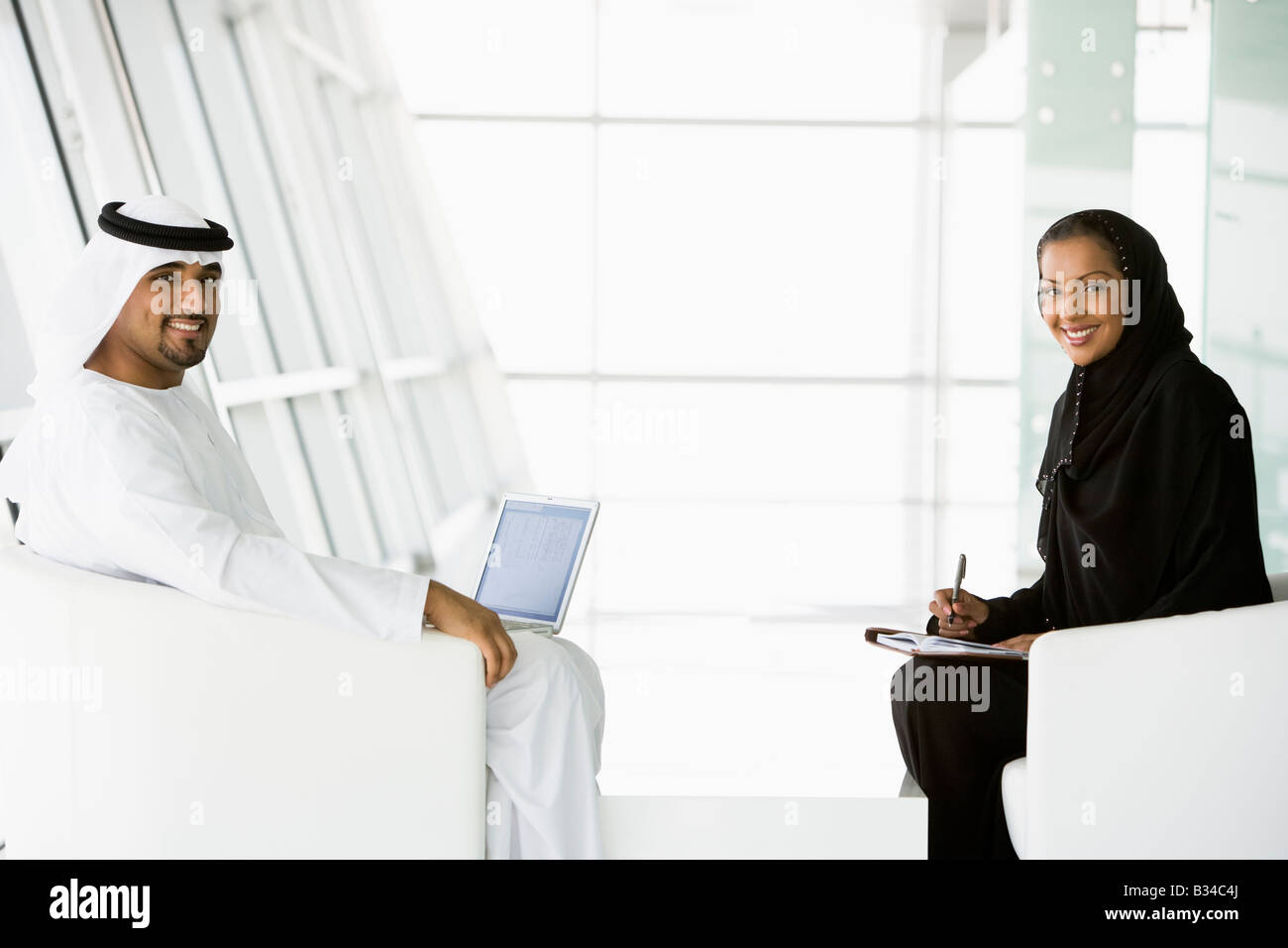 Two businesspeople indoors with a laptop smiling (high key/selective focus) Stock Photo