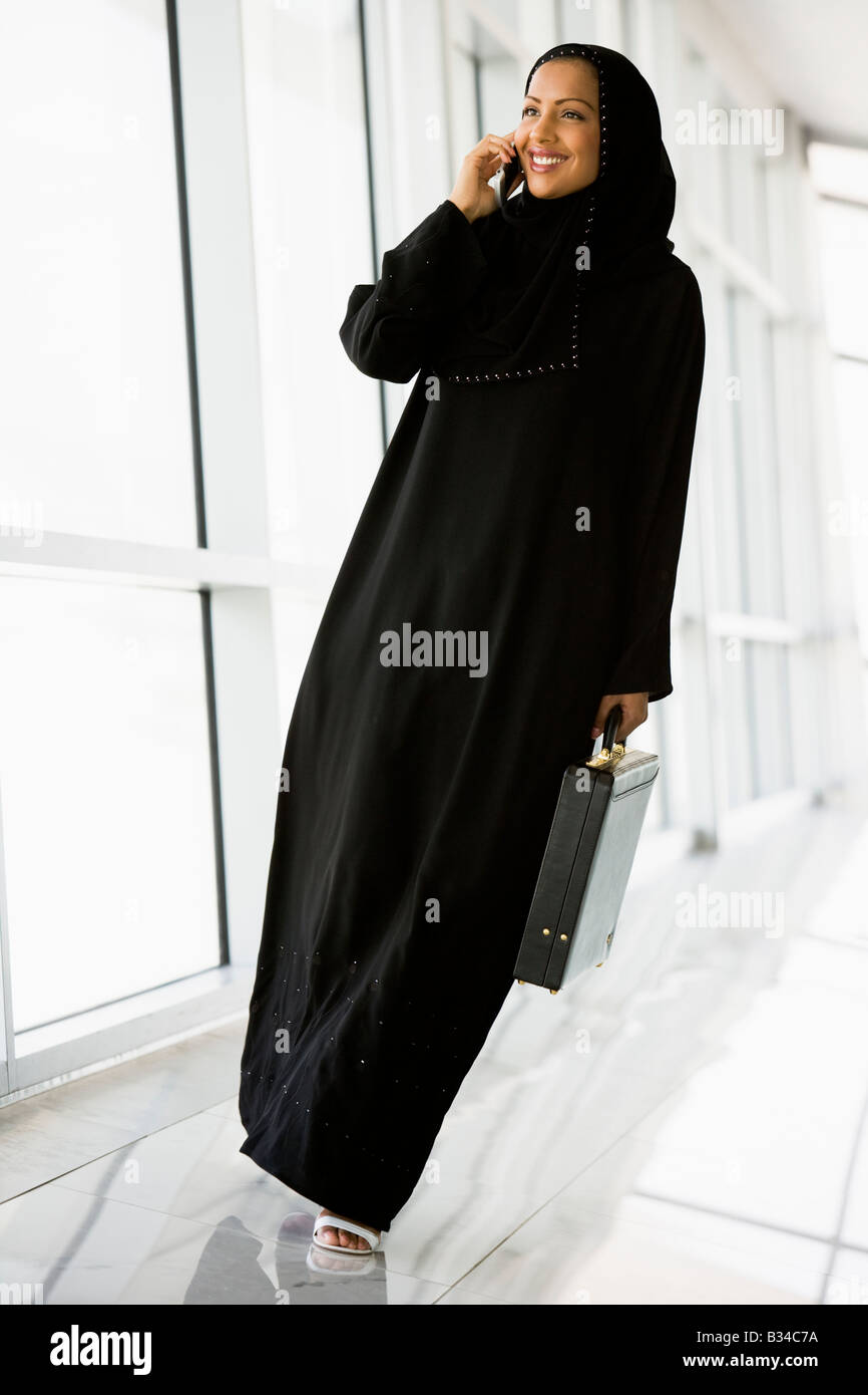 Businesswoman walking in a corridor on a cellular phone smiling (high key/selective focus) Stock Photo