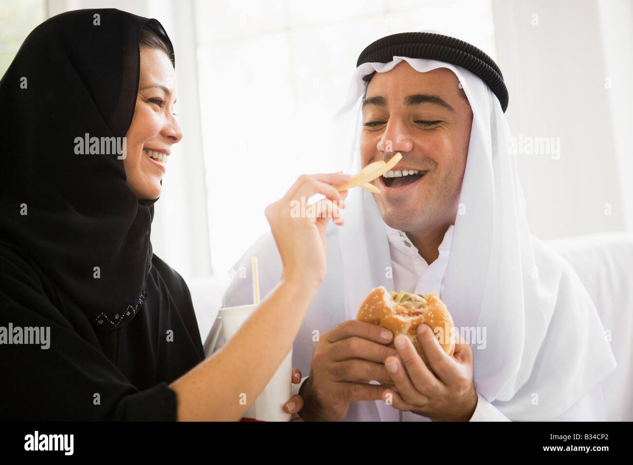 Couple eating fast food in living room and smiling (high key/selective focus) Stock Photo