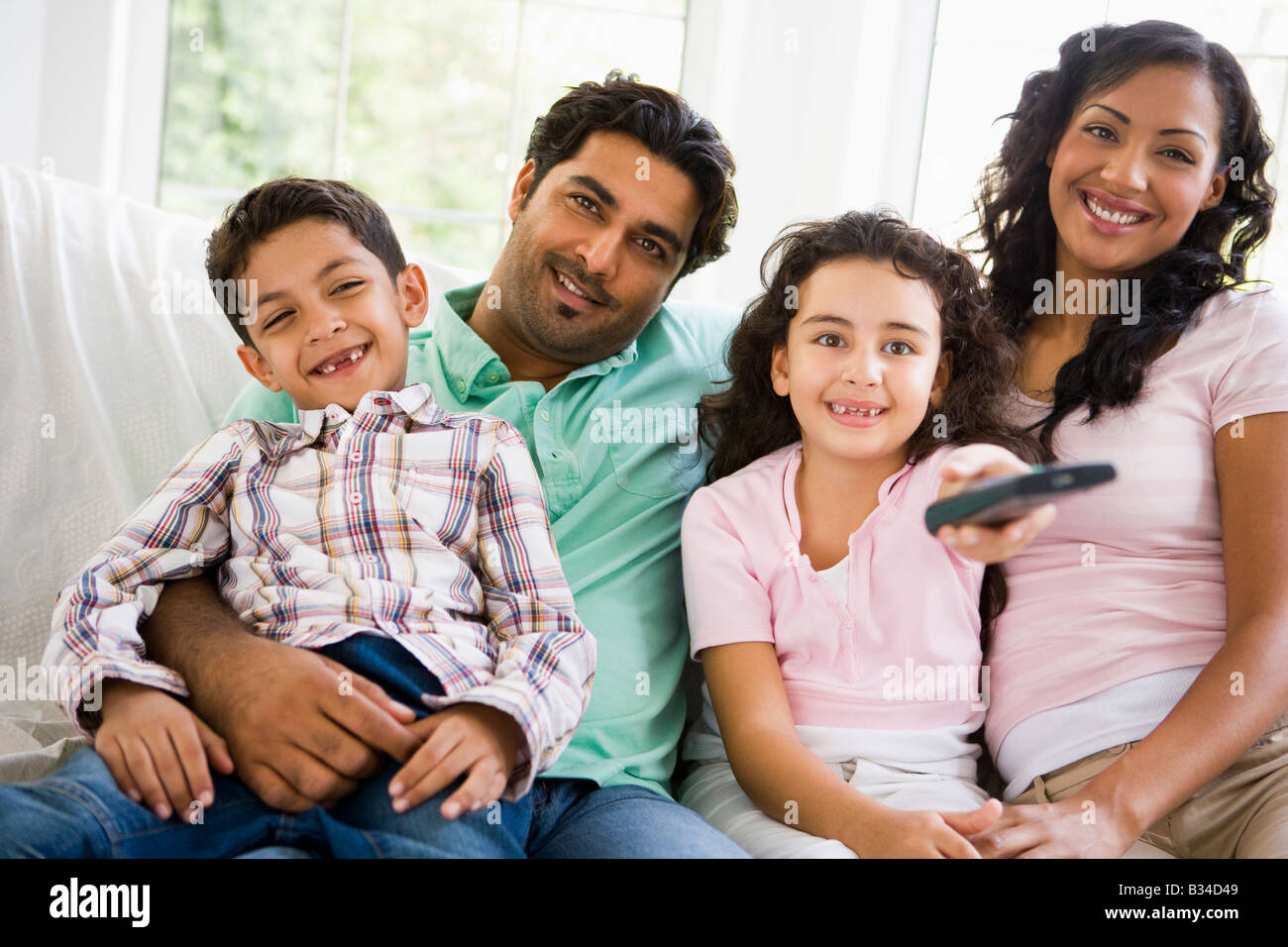Family in living room with remote control smiling (high key/selective focus) Stock Photo