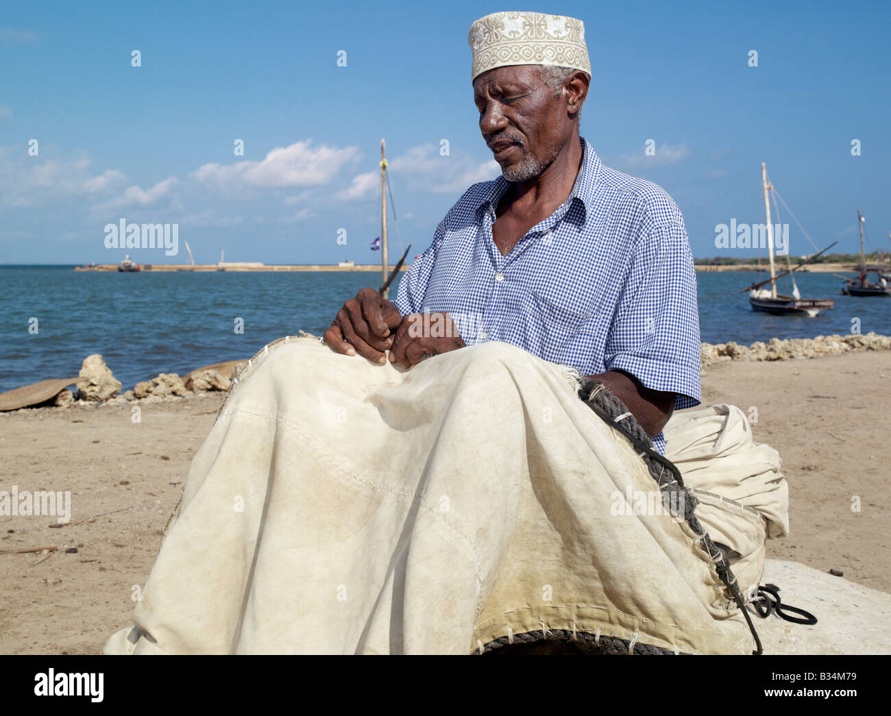 Kenya. A fisherman repairs the sail of his wooden sailing boat, known as mashua, along the waterfront of Kisingitini, a natural Stock Photo