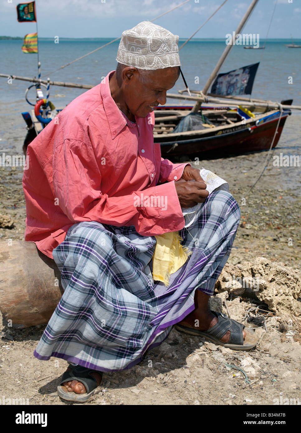 Kenya, Kisingitini, Pate Island. A man embroiders a Swahili hat along the waterfront at Kisingitini, a natural harbour on Pate Island. It takes hours of patience and great skill to finish a really fine hat, which will be prized by Muslims throughout the Lamu Archipelago and elsewhere. Kisingitini is the centre of the island's fishing industry with crayfish being the fishermen's prized catch. The island is the largest of the Lamu Archipelago lying in the Indian Ocean just north of Lamu and 150 miles north-northeast of Mombasa. Stock Photo