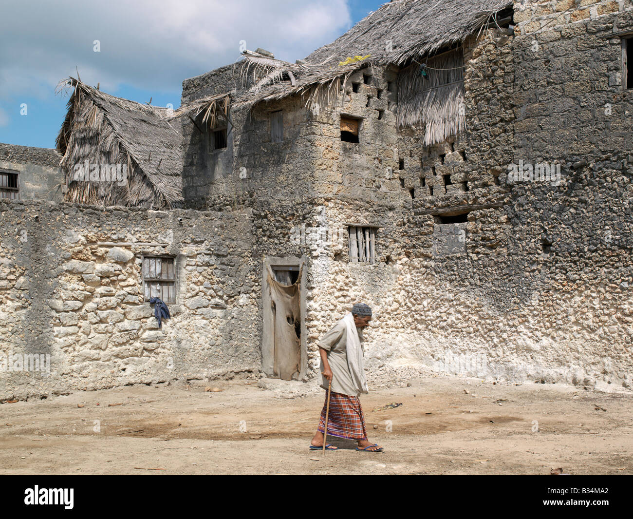 Kenya, Pate Island, Pate Village. An elderly man strides past a large double-storied building in Pate Village. All the buildings Stock Photo