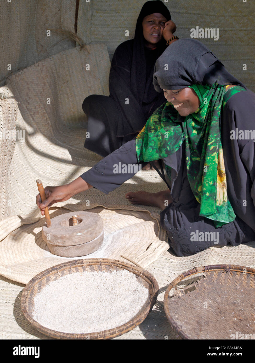 Kenya, Coast Province, Lamu Island. A Swahili woman in Lamu grinds rice using an old hand-operated grinding wheel. Situated 150 Stock Photo