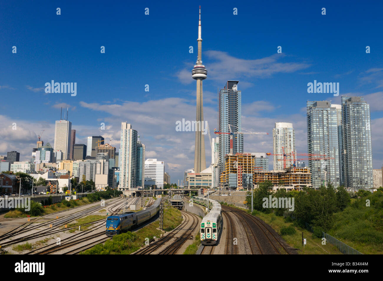 GO and VIA trains leaving downtown Toronto Union Station after work with highrise towers and CN Tower Stock Photo