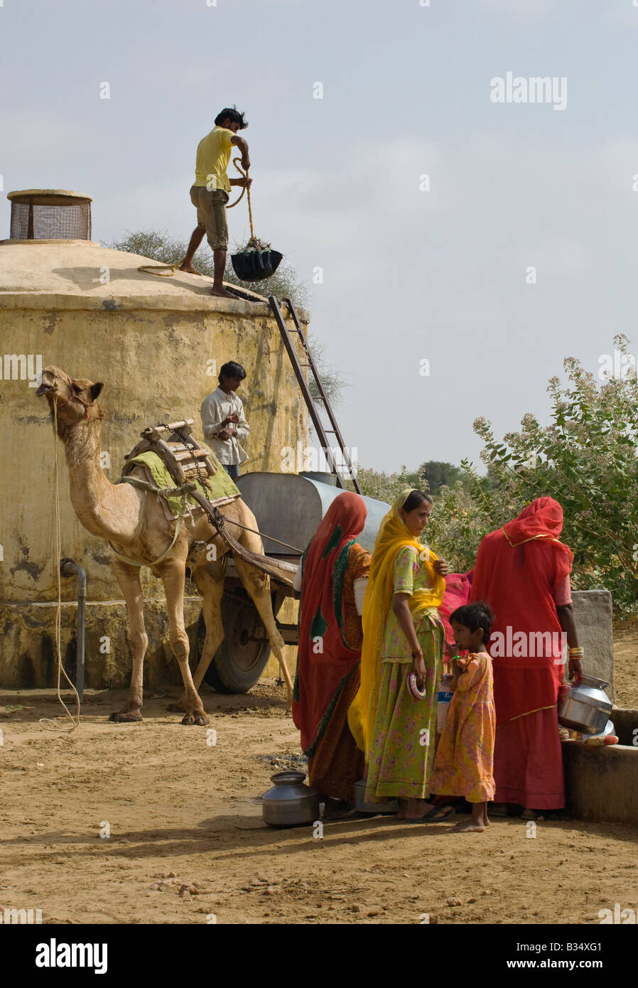 BANJARI TRIBESWOMEN and men with a CAMEL CART gather water at their well in the THAR DESERT near JAISALMER RAJASTHAN INDIA Stock Photo