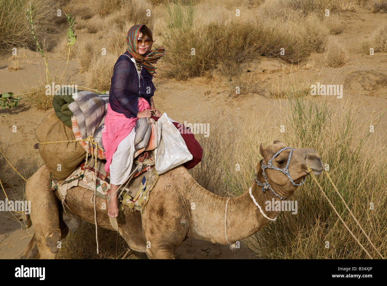 A JAPANESE WOMAN rides a CAMEL in the THAR DESERT during a SAFARI near JAISALMER RAJASTHAN INDIA MR Stock Photo