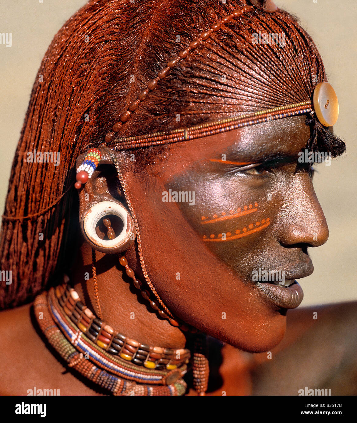 Kenya, Maralal, Maralal. A Samburu warrior resplendent with long, braided, Ochred hair. The round ear ornaments of the warriors are fashioned from ivory. Samburu warriors are vain and proud, taking great trouble over their appearance. Ochre is a natural earth containing ferric oxide which is mixed with animal fat to the consistency of greasepaint. Stock Photo