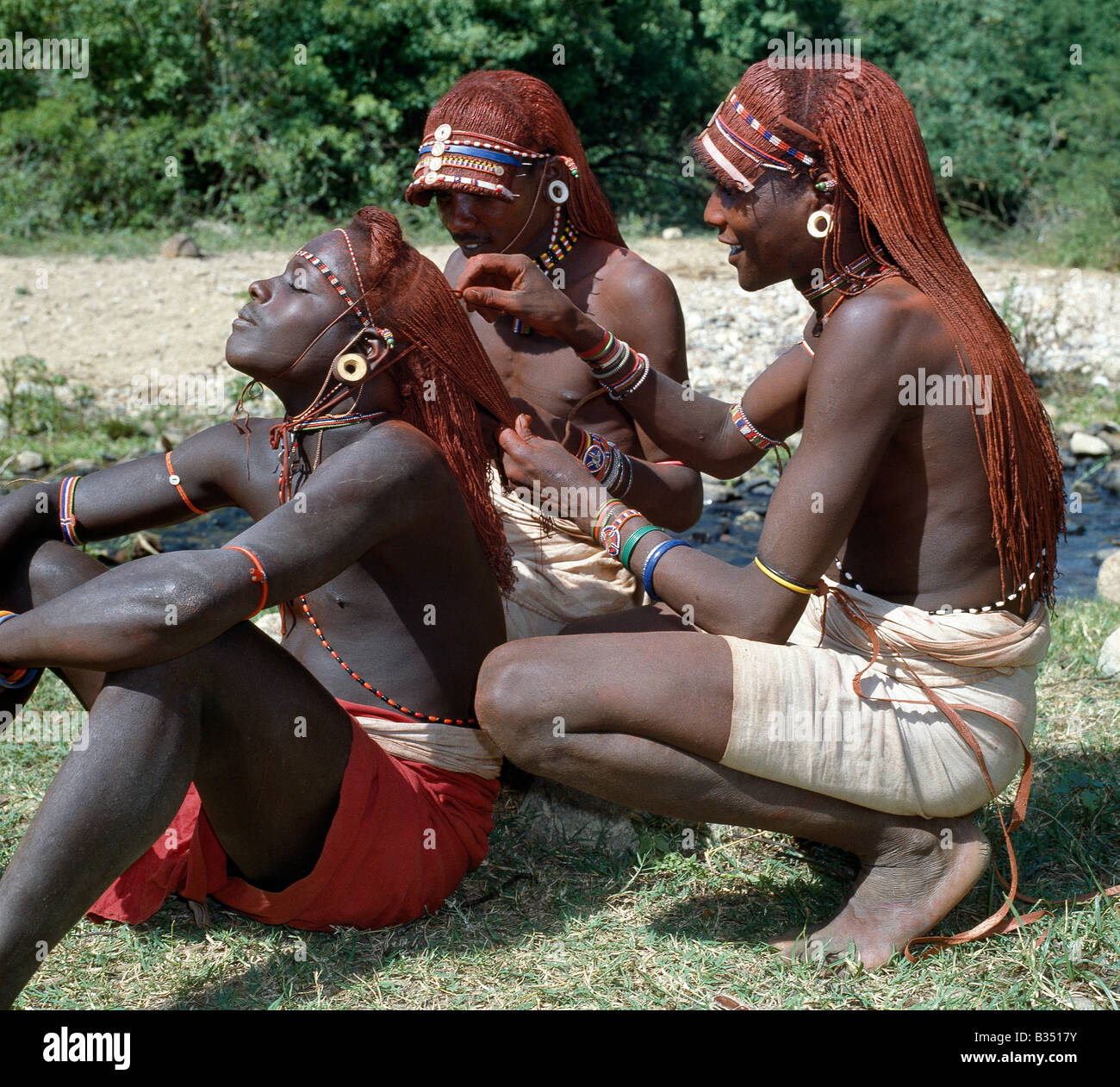 Kenya, South Horr, Kurungu. Two Samburu warriors dress the braids of a colleague. Long braids of Ochred hair. Stock Photo