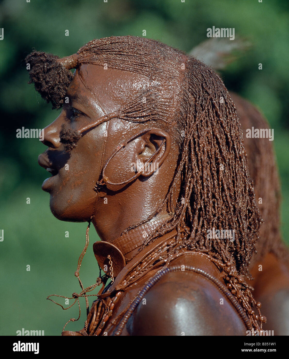 Kenya, Trans-Mara, Lolgorien. A Maasai warrior has daubed himself with red ochre mixed with animal fat to participate in a dance. His long ochred braids have been drawn forward from the crown of the head and tied in three places. This singular hairstyle sets warriors apart from the rest of their society. Stock Photo