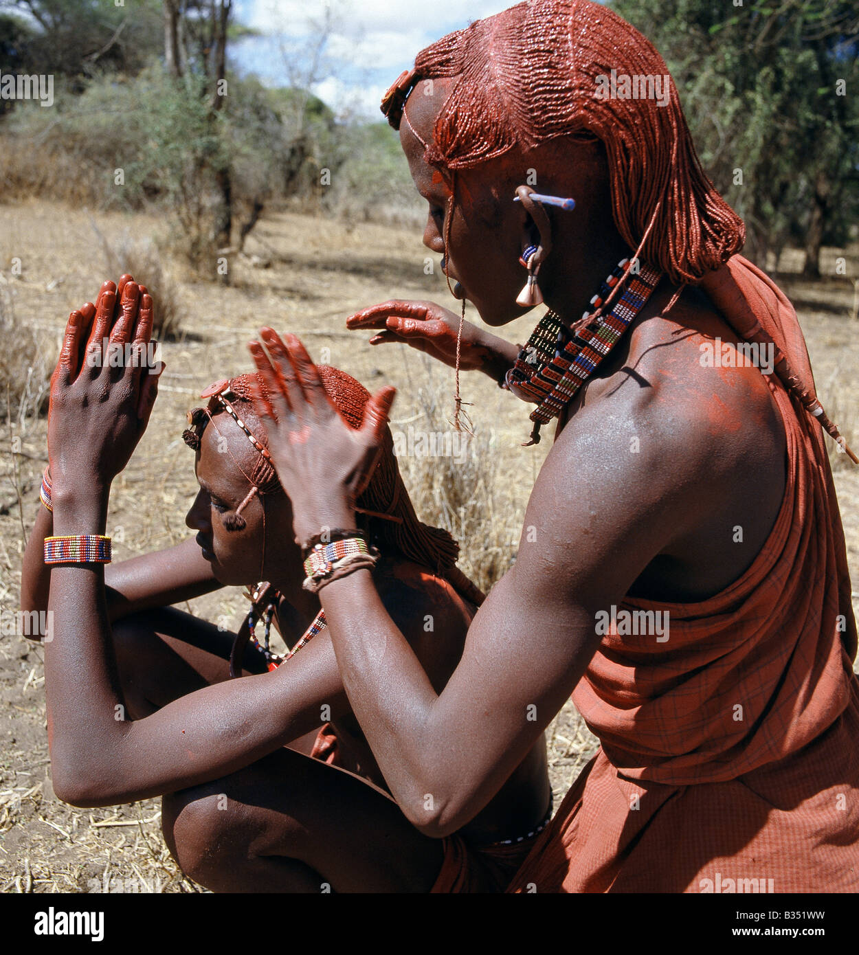 Kenya, Kajiado, Ilbartimaro. A Maasai warrior resplendent with long ochred braids tied in a pigtail at the back, puts red ochre Stock Photo