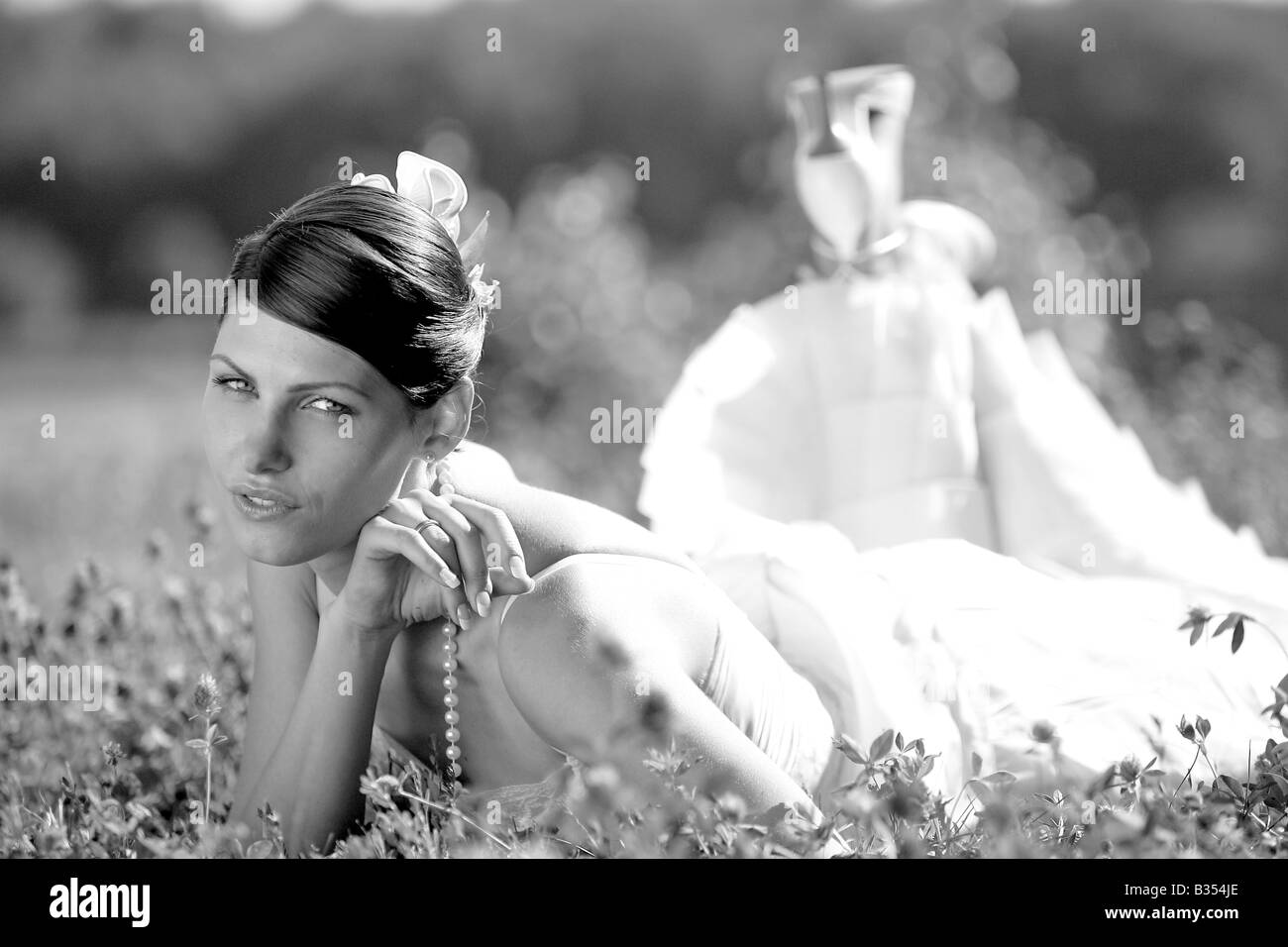 Portrait of beautiful bride in white dress lying down in field. Stock Photo