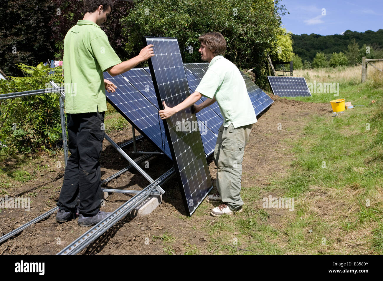 Two workmen installing solar PV panels on galvanised A frame in field Cotswolds UK Stock Photo