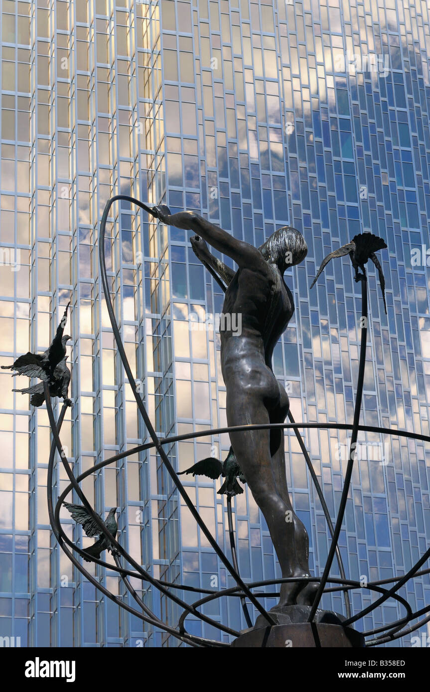 Sculpture of man building global peace with doves against gold glass bank tower reflecting the sky in Toronto Canada Stock Photo