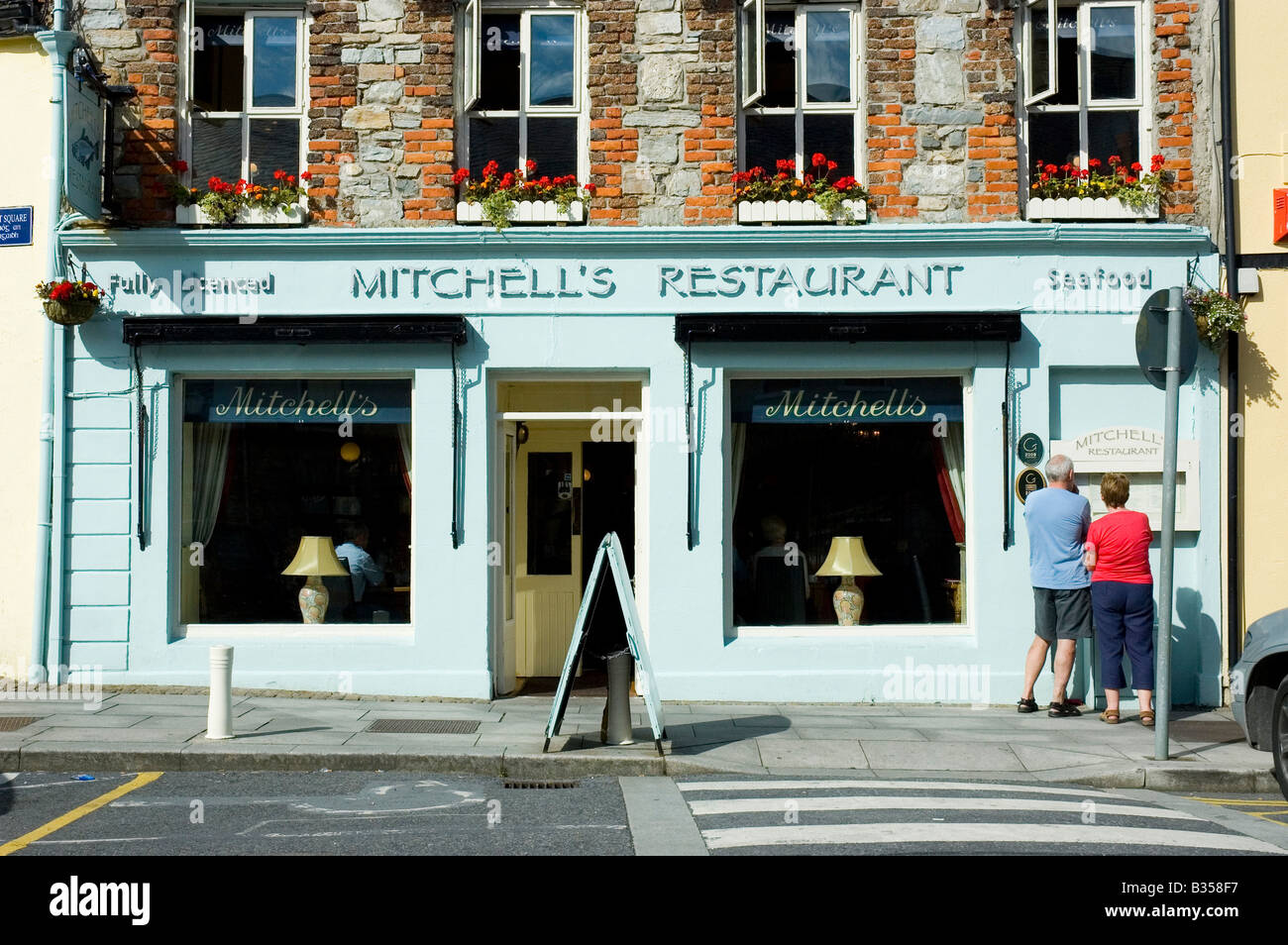 People look at the menu in the window of a restaurant in the town centre of Clifden, Connemara, County Galway, Ireland Stock Photo