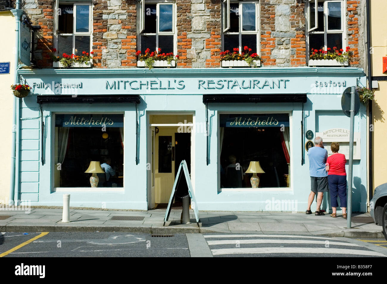 People look at the menu in the window of a restaurant in the town centre of Clifden, Connemara