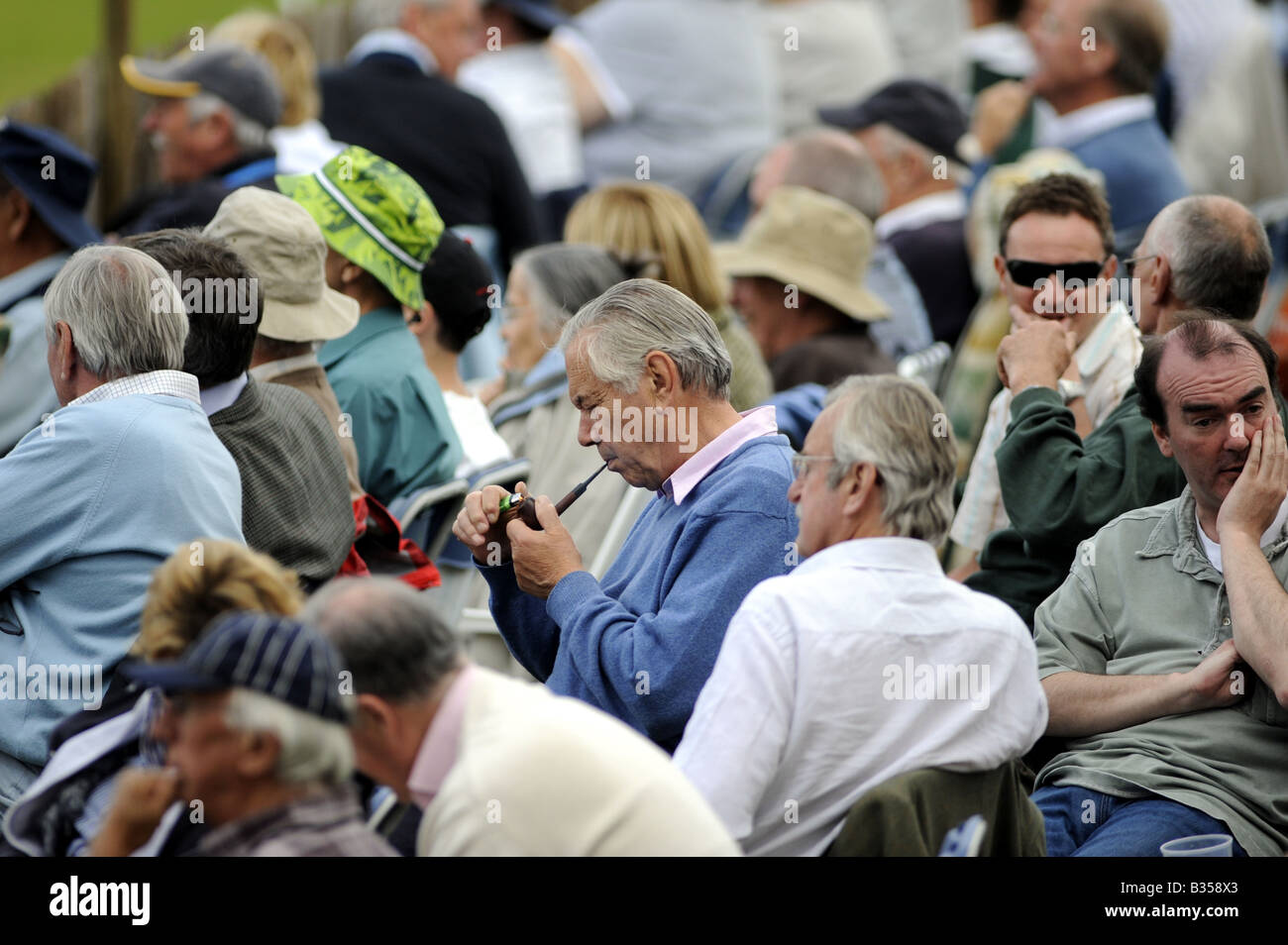 A man lights a pipe amongst a crowd watching cricket at the picturesque Arundel ground in Sussex UK Stock Photo