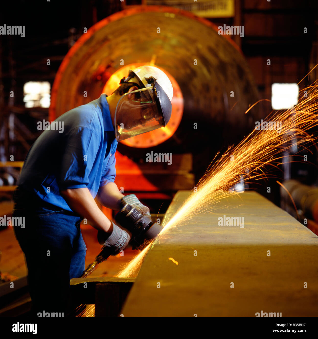 Steel worker grinding metal in a fabrication plant Stock Photo