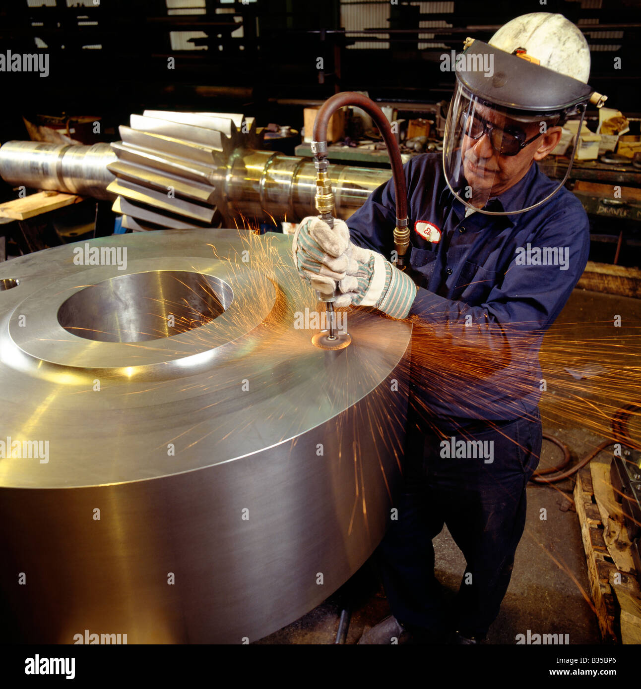 Steel worker grinding metal in a fabrication plant Stock Photo