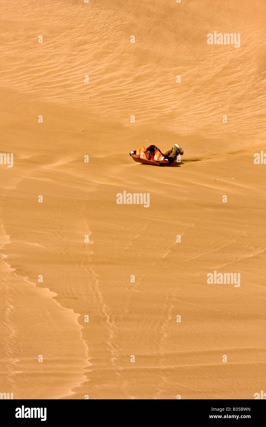 A local man sandboards by sliding down a sand dune on a polished board near Swakopmund a city on
