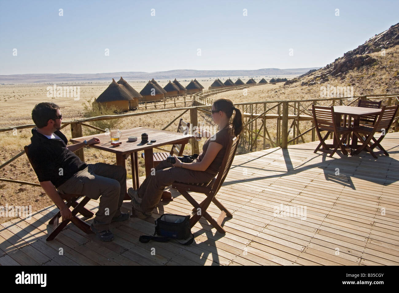 Man and woman enjoy drinks while looking at scenery at Sossus Dune Lodge of Namibia Wildlife Resorts NWR Stock Photo