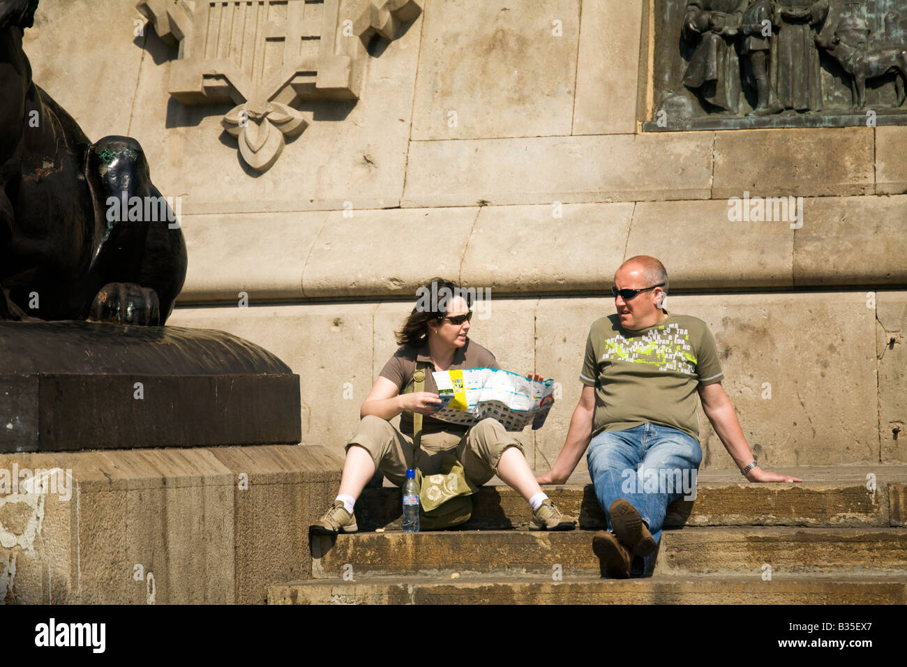 SPAIN Barcelona Young woman hold map and sit with man at base of Christopher Columbus monument to explorer is 200 feet tall Stock Photo