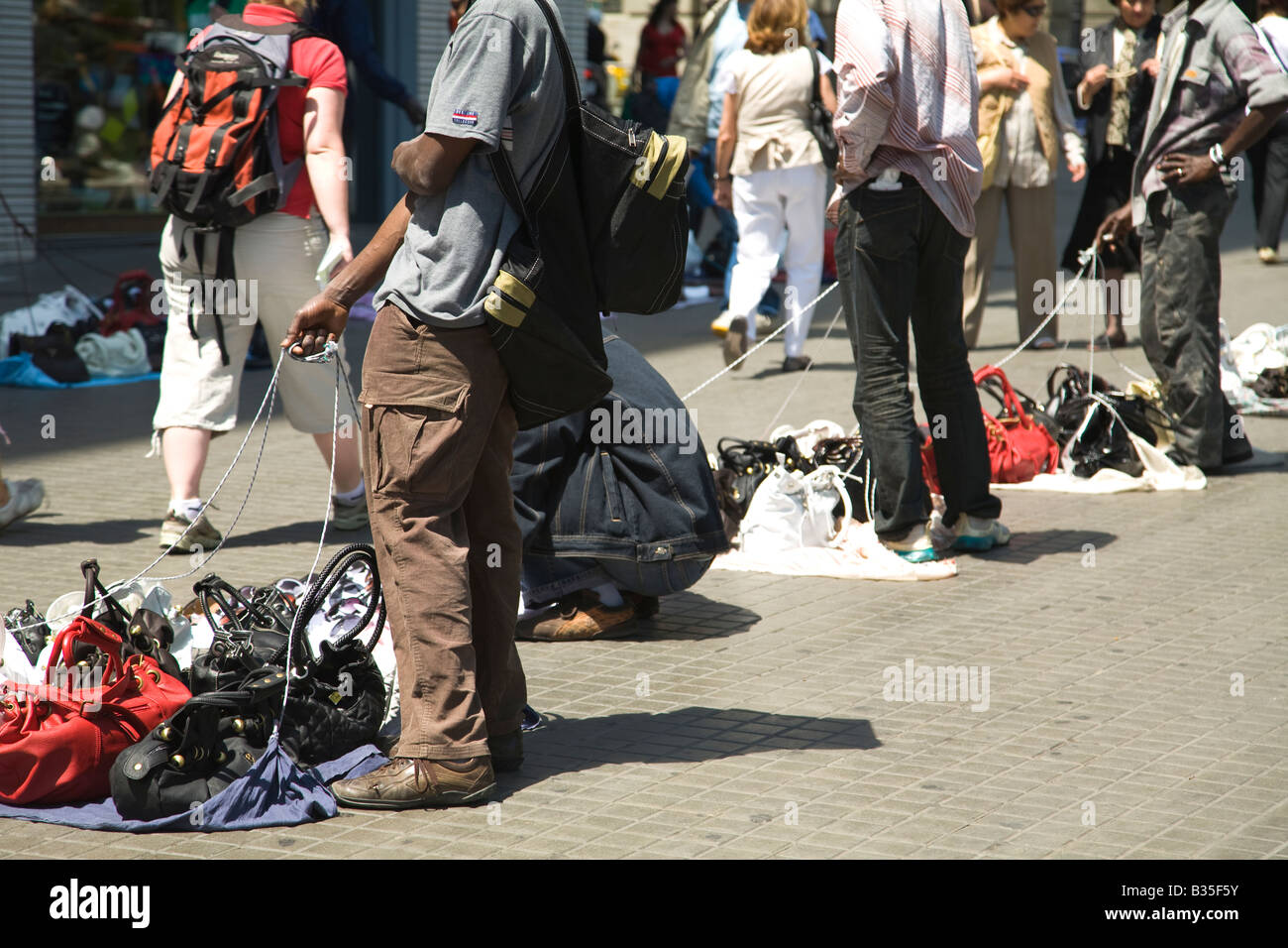 SPAIN Barcelona Street vendors of imitation rip offs and fake items stand on sidewalk customers walk by ready to fold up Stock Photo