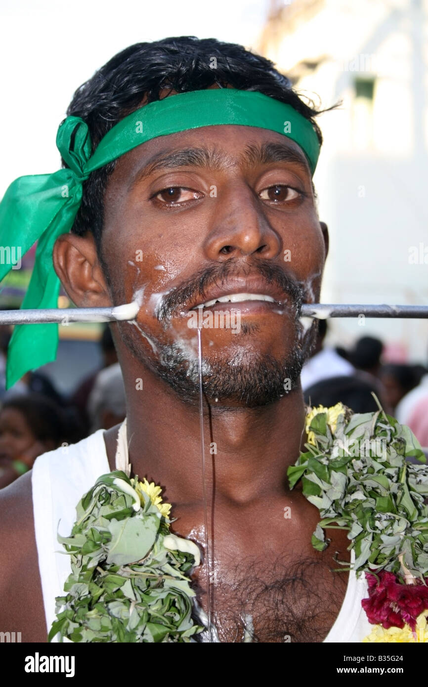 Man parades the street with a large spear through his cheeks in a form of self sacrifice worship to the goddess Mariamman, India Stock Photo